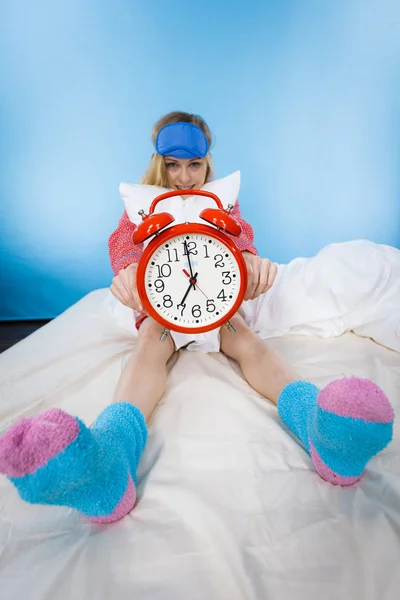 Sleepy woman wearing pajamas holding clock — Stock Photo, Image