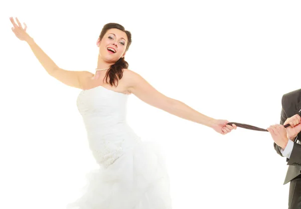 Доминантная невеста в свадебном платье тянет галстук жениха — стоковое фото
