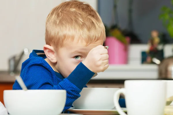 Kid boy äter frukost, flingor och mjölk i skål — Stockfoto