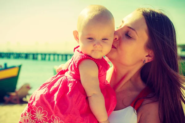Woman kissing baby on beach near water — Stock Photo, Image