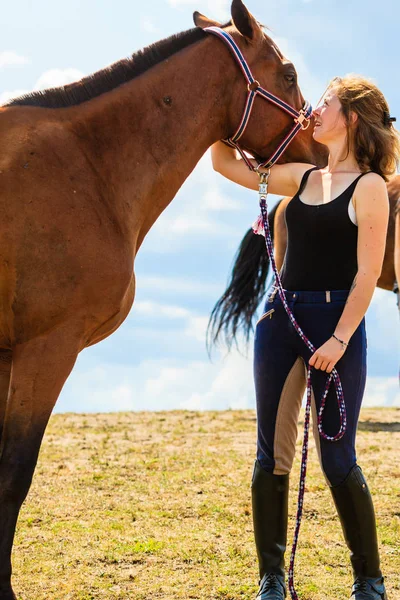 Jockey chica joven besándose y abrazando caballo marrón — Foto de Stock