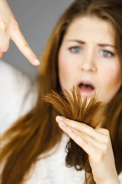 Беспокойная женщина смотрит на свои сухие волосы — стоковое фото