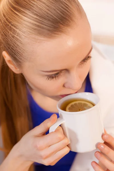 Mujer acostada en un sofá bajo una manta bebiendo té —  Fotos de Stock