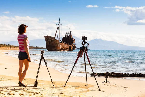 Woman with camera on tripod and shipwreck — ストック写真