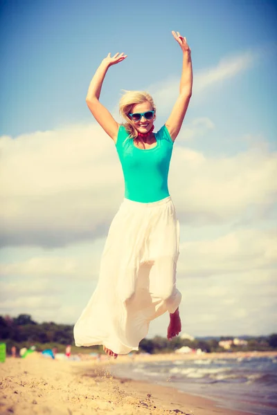 Blonde woman wearing dress playing jumping on beach — Stock Photo, Image