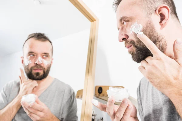 Man applying moisturizer cream in bathroom
