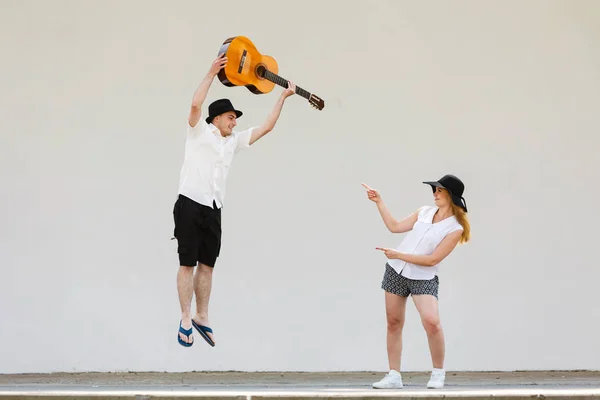 Man jumping with guitar, woman pointing at him — Stock Photo, Image