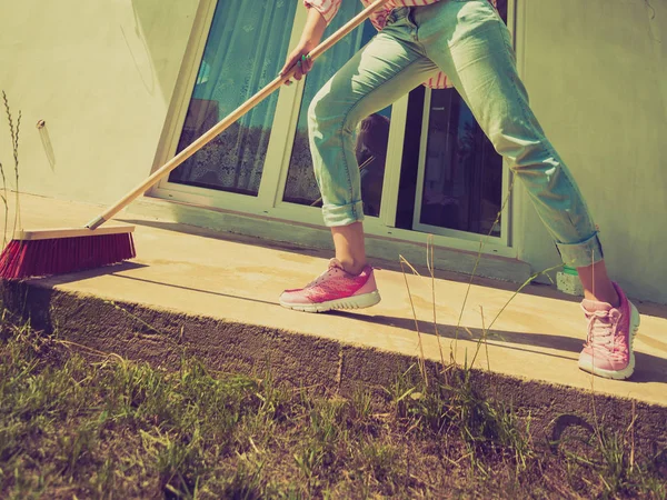 Woman cleaning patio using brush broom