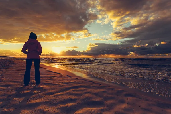 Kobieta ciesząca się dramatycznym zachodem słońca na morzu — Zdjęcie stockowe
