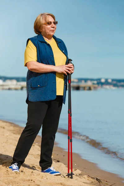 Senior woman practicing nordic walking on beach — Stock Photo, Image