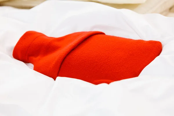 Botella de agua caliente roja caliente sobre ropa de cama blanca —  Fotos de Stock