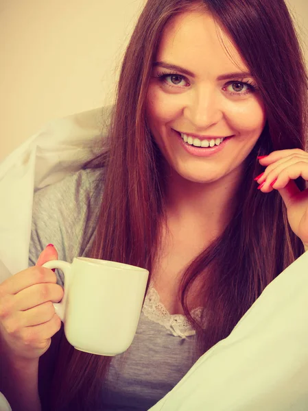 Femme souriante tenant une tasse de boisson au lit — Photo