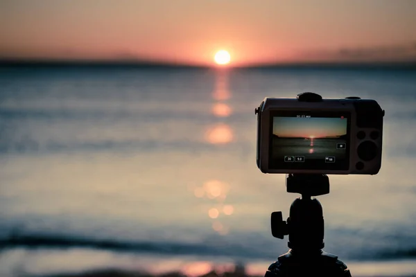 Cámara tomando fotos de la salida del sol sobre la superficie del mar — Foto de Stock