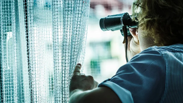 Man met verrekijker die buren bespioneert — Stockfoto