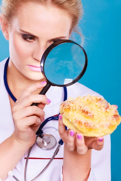 Doctor with magnifying glass examining sweet food — Stock Photo, Image