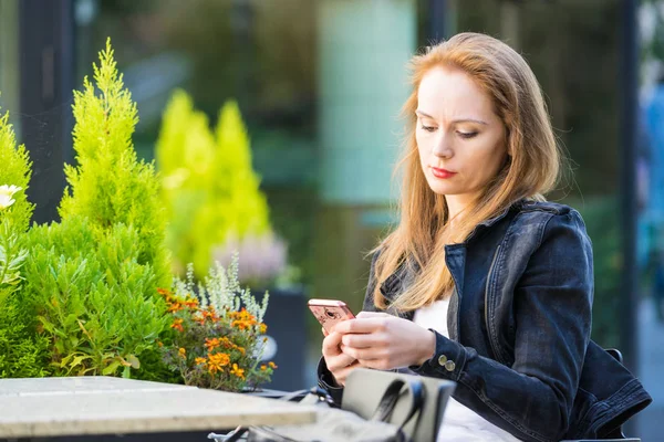 Женщина ждет в открытом кафе, смотрит на сотовый телефон — стоковое фото