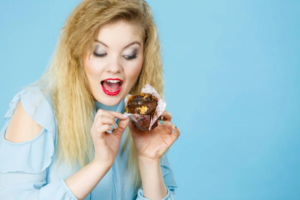 甘い食べ物の砂糖は私たちを幸せにします 魅力的なブロンドの女性が持っていますおいしいチョコレートカップケーキで手 口を開けて ケーキのために渇望 — ストック写真