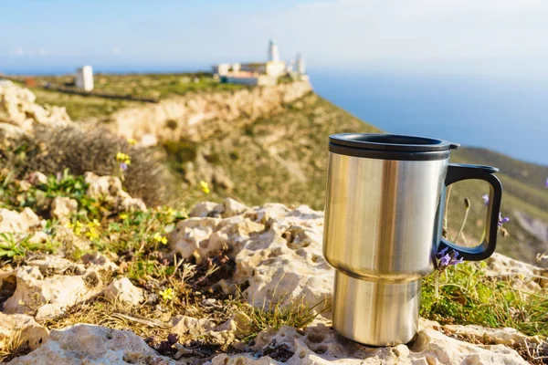 Thermal mug, thermos on nature. Travel destination, Mesa Roldan lighthouse in the background. Camping, vacation, lifestyle concept.