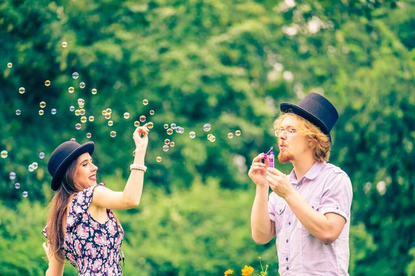 幸せな面白いですヒップスターカップル遊び一緒に吹いて石鹸泡屋外で春の公園 — ストック写真
