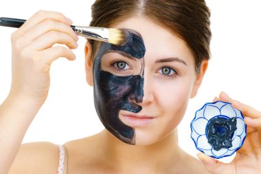 Woman applying with brush clay carbo detox black mask to her face, on white. Girl taking care of oily skin complexion. Beauty treatment. Skincare. clipart