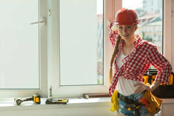 Pretty young woman construction worker with helmet about to fix window picking best tools. Working at flat remodeling. Building, repair and renovation.