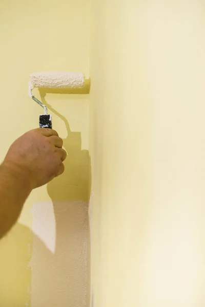 人们用滚筒刷把白色油漆涂在黄色的墙上 家庭翻新概念 — 图库照片