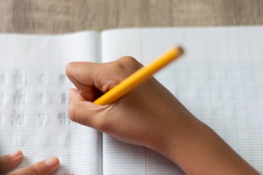 Ödev yapmak küçük bir kız. El sarı bir kalem tutan ve bir defter ile yüksek açı yazma. Odak sığ alan derinliği ve bulanık arka plan seçin.