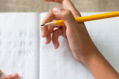 Ödev yapmak küçük bir kız. Elini yüksek açı ile sarı bir kalem tutuyor. Odak sığ alan derinliği ve bulanık arka plan seçin.