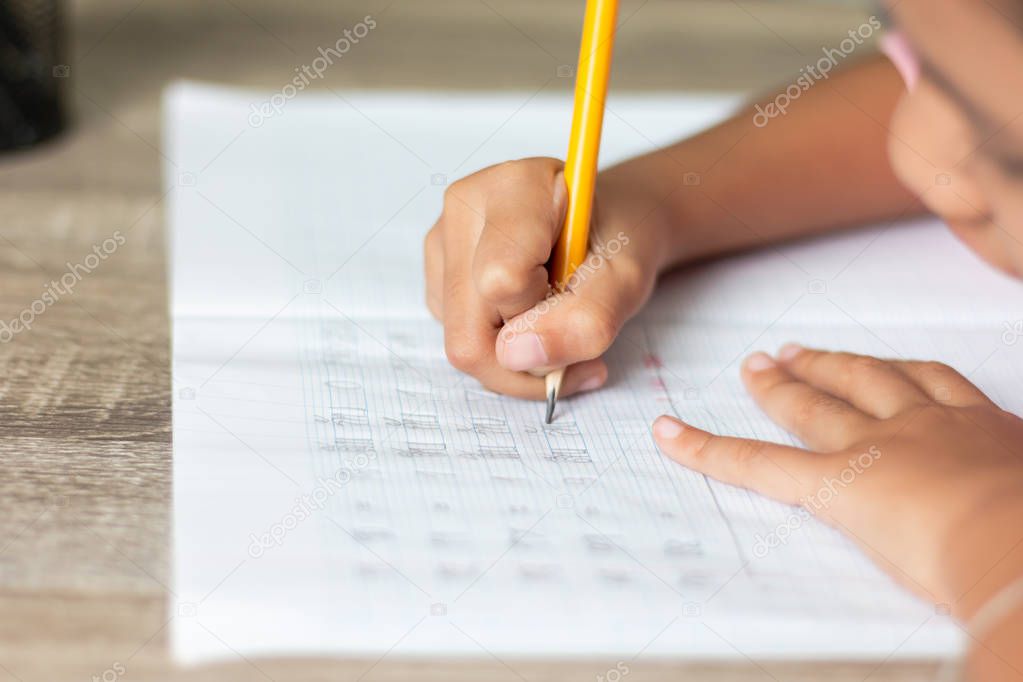 Close up a little girl doing homework. Hand is holding a yellow pencil and writing in a notebook. Select focus shallow depth of field and blurred background with copy space.