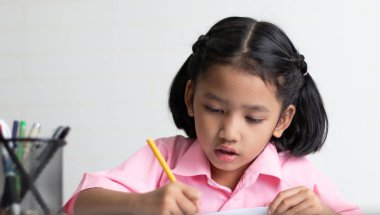 Yakın yukarı küçük kız dikkatle ev ödevi yapıyor. Çocuklar kullanım sarı bir kalem bir defter yazıyor. Beyaz arka plan üzerinde kopya alanı ile alan odak sığ derinliği seçin.