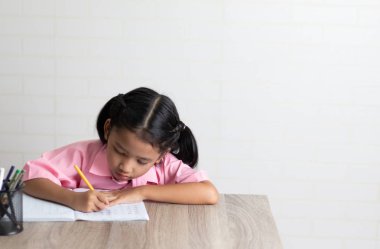 Küçük kız dikkatle ev ödevini yapıyor. Çocuklar ahşap masaya bir defter yazan sarı bir kurşun kalem kullanıyor. Beyaz arkaplanda kopyalama alanı olan yüzeysel alan derinliğini seç.