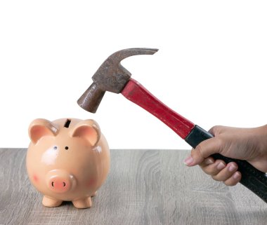 Ahşap masa gri arka plan üzerinde bir kumbara parçalamak için paslı bir çekiç bir kadın tutar.