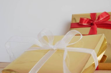 Ahşap masa ve beyaz arka plan kırmızı kurdele ile altın hediye kutuları.