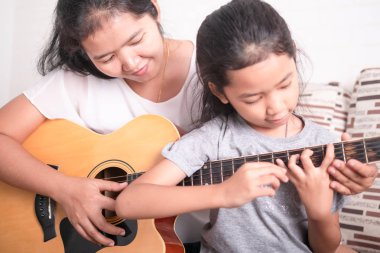 Anne kızına gitar çalmayı öğretiyor..