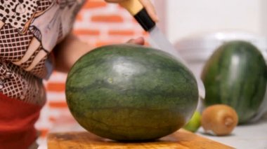 Mutfakta ki tahta tahtanın üzerine karpuz yarısını kesen bıçak kullanan kadınların elleri