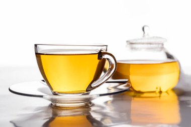 Bir fincan taze demlenmiş çay şeffaf bardakta ve masada yansımalı çaydanlık..