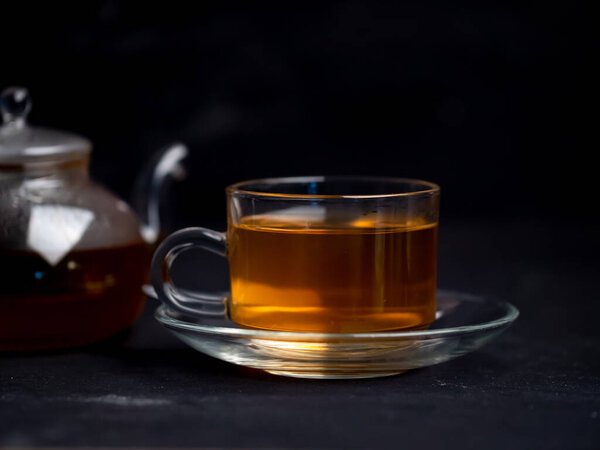 A cup of freshly brewed hot tea and a teapot on the table with a black backgrounds.