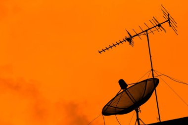 Televizyon anteni ve uydu çanağı iletişim için günbatımı gökyüzü ile çatıda twilight saat, siluet turuncu arka plan, kopya alanı ile etkisi ışık yayın.