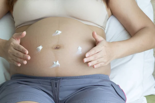 Pregnant woman hands lotion help skin belly on bedroom background, healthy concept.