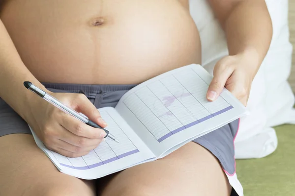 Pregnant woman record in note book in bedroom background, healthy concept.