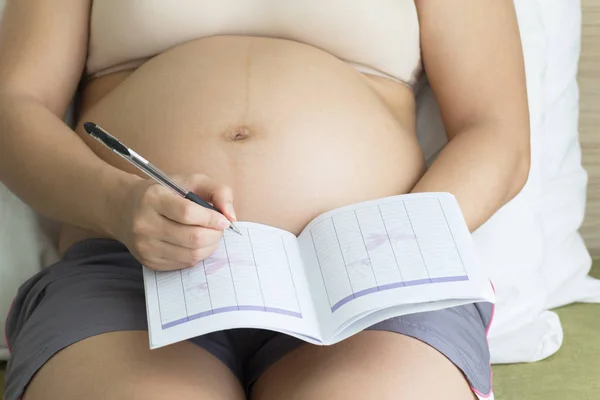 Pregnant woman record in note book in bedroom background, healthy concept.