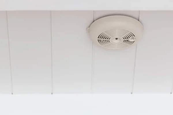 Smoke detector of fire alarm on white wooden ceiling.