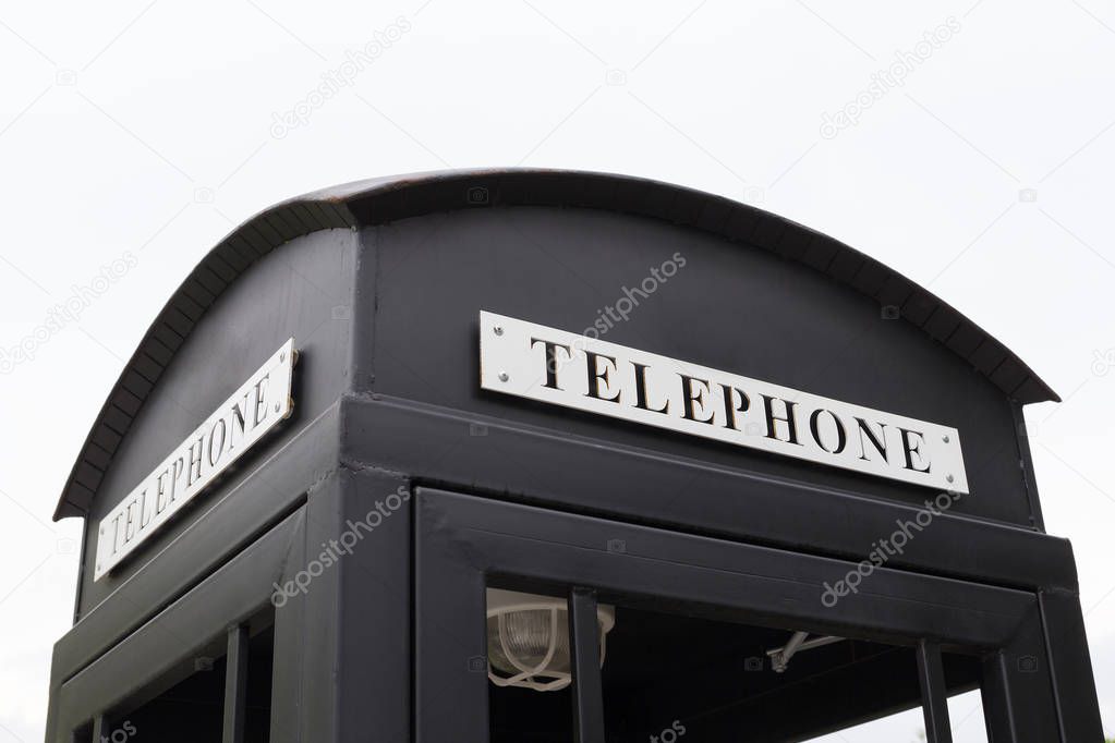 Vintage big black pay phone on white sky.