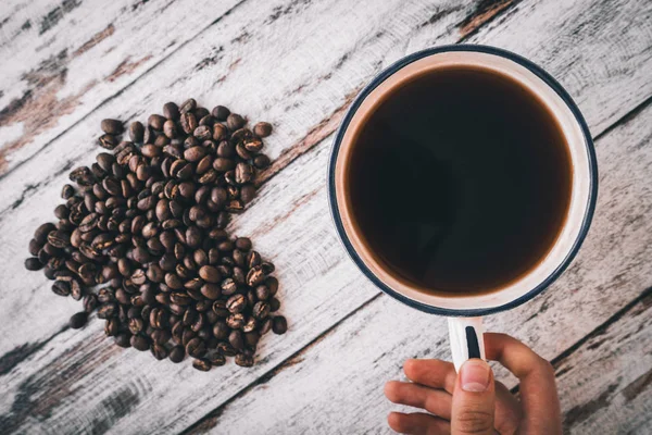 hand holding cup of coffee with heart from coffee beans on table