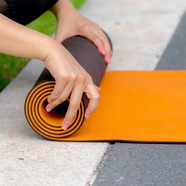 Outdoor yoga practice, in the midst of nature, is a very good meditation practice for self,Use your hands to hold a yoga mat with a cylindrical roll, orange and dark brown.