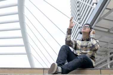 Zaman zaman mutlu veya o zaman Asyalı erkek Bluetooth kulaklık, siyah çerçeve gözlük, koymak zihin iyileştirmeye yardımcı olur orta müziktir kamuoyunda müzik dinlemek.