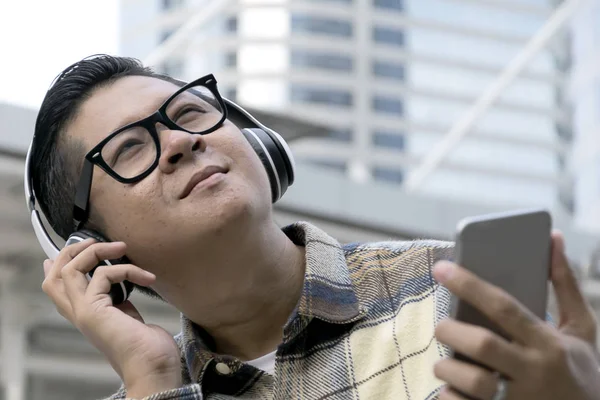 Music is the medium that helps to heal the mind,When the time is happy Or at the time,Asian men put Bluetooth Headphones,black frame glasses,Listening to music in public.