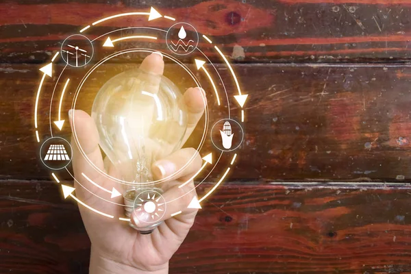 Hand holding light bulb in front of global show the world's consumption with icons energy sources for renewable, sustainable development. Ecology concept.