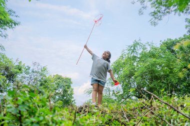 Asyalı bir kız, geniş bir dünyada macera yaşıyor. Bir böcek yakalayıcıyla bir tepede durur ve böcekleri yakalamaya hazırdır.