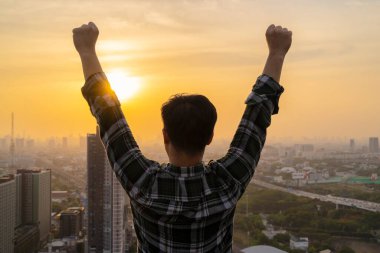 Asyalı işadamı yüksek bir binanın üzerinde duruyor. Başarının gururunu ifade etmek, günbatımı geçmişi. İş kazananı ödülü